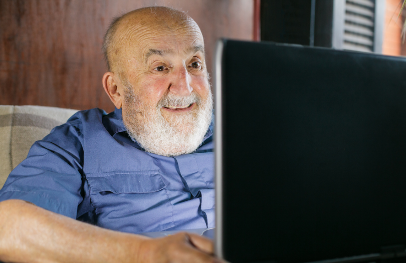 Older white man with beard man happily using laptop