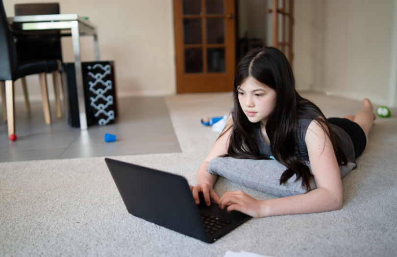 Teenage girl at laptop on living room floor surrounded by toys